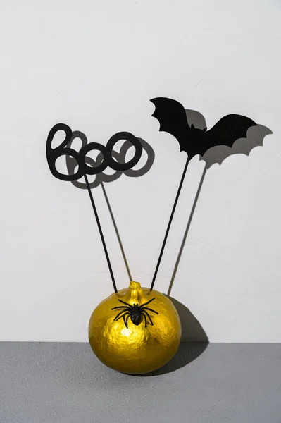 Halloween decorations. Painted golden pumpkin with scary black Halloween objects with shadows on a gray background.