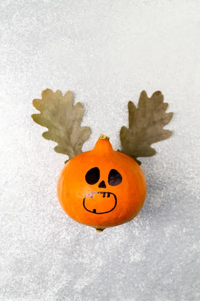 Top view Halloween pumpkin with painted face and horns made from autumn leaves on a shiny silver background. — Stock Photo, Image