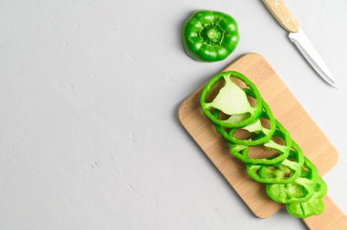 Eko gıda konsepti. Kesme tahtasında dilimlenmiş yeşil biber ve bıçak manzarası. Açık gri arkaplan. Asgari biçim.