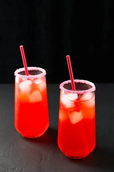 Des moquettes d'été rafraîchissantes avec des glaçons. Deux grands verres de jus rouge glacé avec des pailles sur fond sombre. — Photo