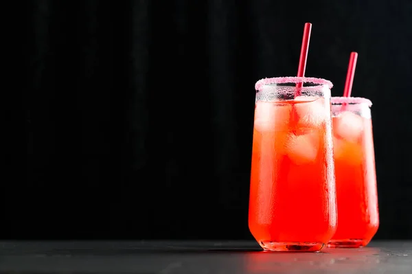 Des moquettes d'été rafraîchissantes avec des glaçons. Deux grands verres de jus rouge glacé avec des pailles sur fond sombre. — Photo