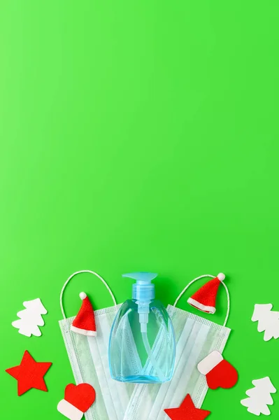 Top view of medical masks, sanitizer bottle, and Christmas decorations on green background. — Stock Photo, Image