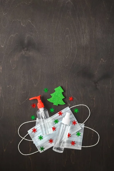 Medical protective masks, sanitizer bottles and Christmas decorations on a dark brown background.