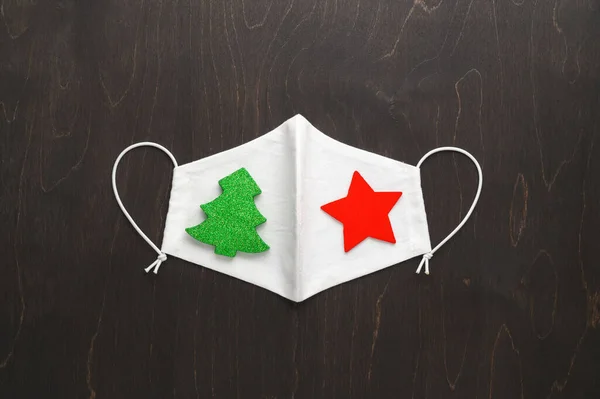 Conceito vívido da era do Natal. Máscara de rosto de pano reutilizável decorada com decorações de Natal em um fundo marrom escuro. — Fotografia de Stock