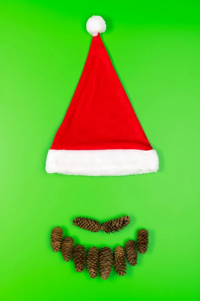 Rosto de Papai Noel feito de cones de abeto e um chapéu vermelho tradicional em um fundo verde. Conceito mínimo de Natal. — Fotografia de Stock