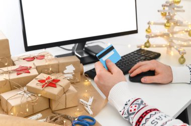 İnternetten Noel alışverişi. Tanımlanamayan Adam Eller kredi kartı tutuyor ve bilgisayar kullanarak hediyeler alıyor..
