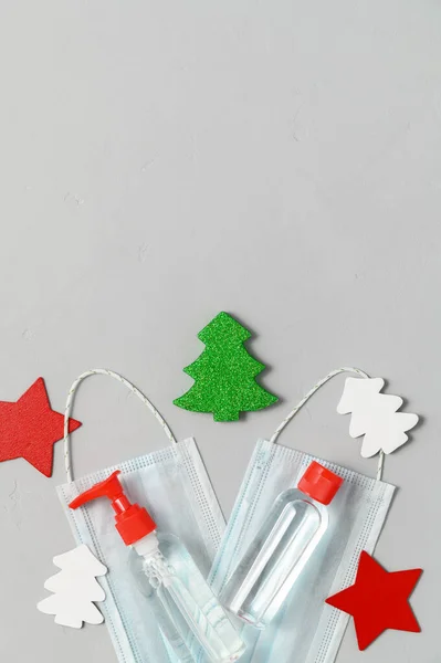 Medical protective masks, sanitizer bottles and Christmas decorations on a gray background.