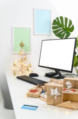 Kredi kartıyla Noel alışverişi. Noel hediyeleri ve ev ofisindeki bir masada bilgisayar monitörü..