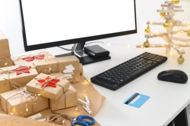 Kredi kartıyla Noel alışverişi. Noel hediyeleri ve ev ofisindeki bir masada bilgisayar monitörü..