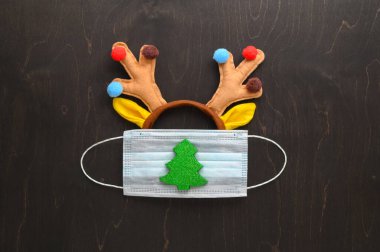 Noel 'de çok yönlü bir kavram. Koyu kahverengi arka planda tıbbi koruyucu maske ve Noel süslemeleri..