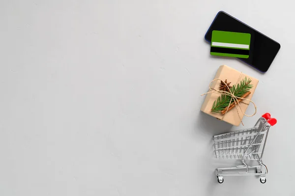 Concept d'achat en ligne. Vue du dessus du smartphone, carte de crédit, chariot d'achat et boîte cadeau sur fond gris clair. — Photo