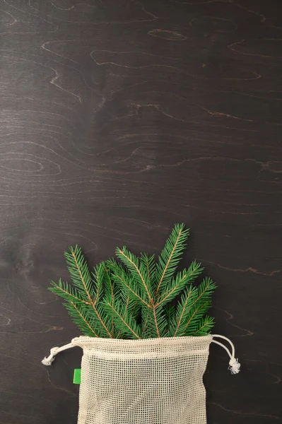 Buquê de ramos de abeto em saco ecológico de tecido em fundo marrom escuro. Conceito mínimo de resíduos de Natal zero. — Fotografia de Stock