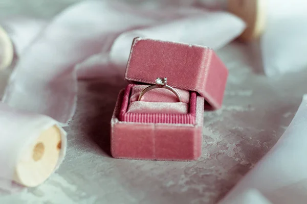 romantic present: pink velvet box with a wedding ring and light satin ribbons on a gray background