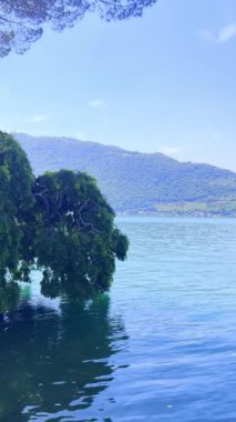 İtalya 'daki mavi gökyüzünü yansıtan sakin bir Iseo gölünün olduğu çarpıcı bir manzara. Yeşillik tarafından çerçevelenmiş görkemli dağlar uzaklardan yükselir. Huzurlu ve görkemli bir manzara yaratır..