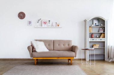 Açık büfesi olan, geniş, parlak bir oturma odasında bej renkli beyaz yastıklı şık bir kanepe.