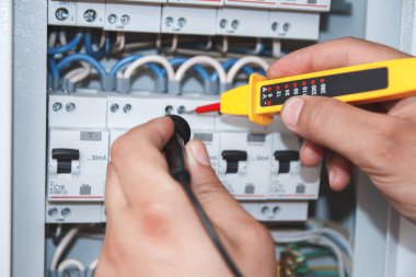 Hands of electrician with multimeter probe at an electrical switchgear cabinet examining fuse box clipart