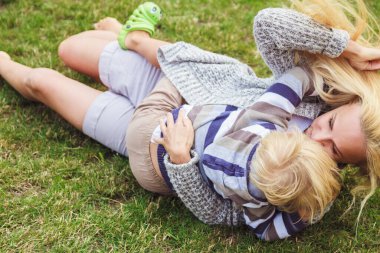 Küçük tatlı bir oğlu olan genç bir anne bir kır evinin yeşil çimlerinde sarılıp eğleniyor.