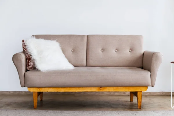 Stylish beige sofa with a white fluffy pillow against a white wall background