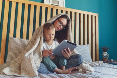 Evlerinin yatak odasında battaniyenin altında bir tabletle genç anne ve oğul.