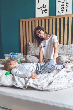 Anne ve bebek yatakta birlikte eğleniyorlar.