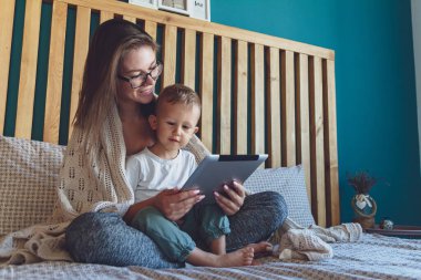 Evlerinin yatak odasında battaniyenin altında bir tabletle genç anne ve oğul.