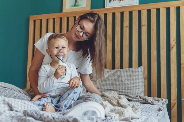 Oğlu olan bir kadın evdeki yatak odalarında nebulizörle solunum yapıyor.