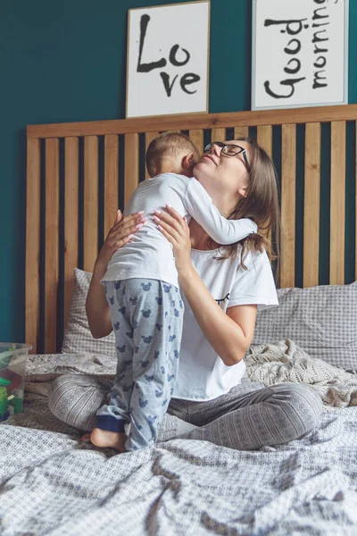 Anne ve bebek yatakta birlikte eğleniyorlar.