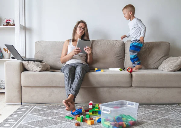 孩子们在沙发上玩耍，而妈妈则在玩平板电脑、杂物和玩具。 — 图库照片