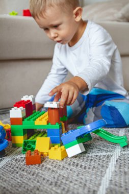 Çocuk yerde oturmuş oyuncak bloklarıyla oynuyor.
