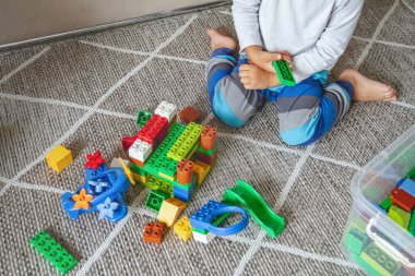 Çocuk yerde oturmuş oyuncak bloklarıyla oynuyor.