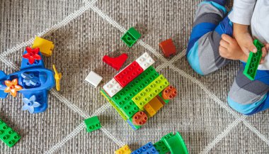 Çocuk yerde oturmuş oyuncak bloklarıyla oynuyor.