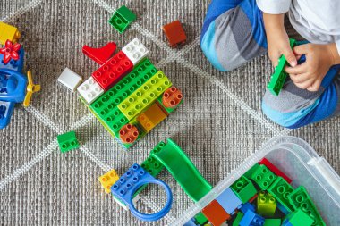 Çocuk yerde oturmuş oyuncak bloklarıyla oynuyor.