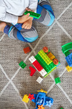 Çocuk yerde oturmuş oyuncak bloklarıyla oynuyor.