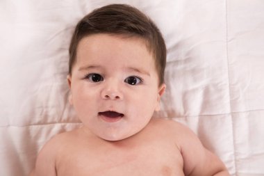 Üstten görünüm ve yakın çekim portre sevimli bebek çocuk yatak kameraya bakıyor. Rahatlatıcı ve çocuk odasında yatakta gülümseyen yeni doğan çocuk