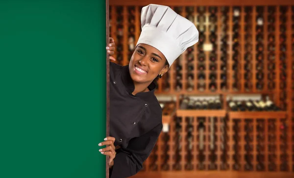 Black Brazilian woman chef cooking looking at camera with green board in wine house blurred background