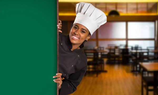 Black Brazilian woman chef cooking looking at camera with green board in wine house blurred background