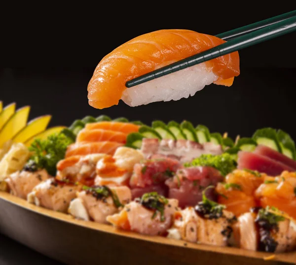 close up salmon nigiri in hashi with Japanese food combo defocused in black background.