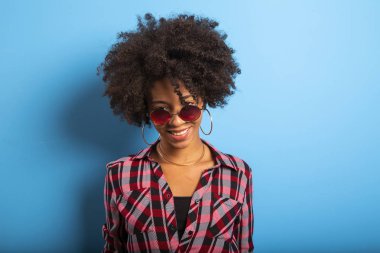 Neşeli çekici afro brezilyalı kız mavi duvar arka planda güneş gözlüğü giyen hayatın tadını çıkarın - Imagem.