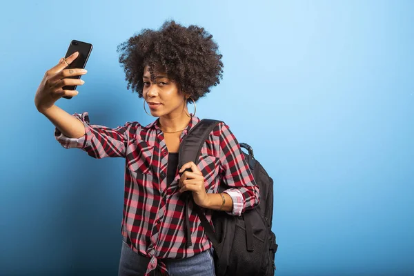 Primer plano retrato de la joven sonriente atractiva mujer brasileña africana sosteniendo teléfono inteligente, tomando foto selfie en el fondo azul . — Foto de Stock