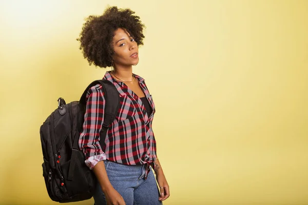 Joven estudiante africano con mochila en la espalda sobre fondo amarillo . — Foto de Stock