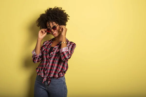 Chica brasileña afro atractiva alegre disfrutando de la vida usando gafas de sol Sobre fondo amarillo de la pared - Imagem . — Foto de Stock