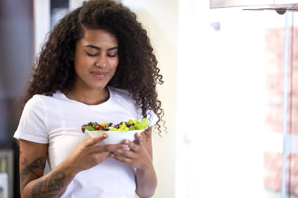 Allegro giovane afro americano donna mangiare insalata di verdure in cucina a casa . — Foto Stock