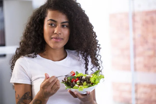 Allegro giovane afro americano donna mangiare insalata di verdure in cucina a casa . — Foto Stock