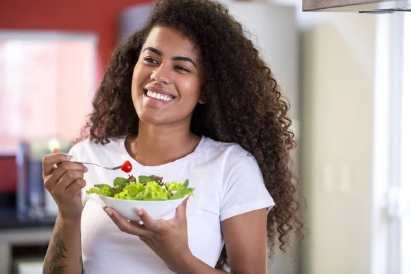 Cheerful young afro american woman eating vegetable salad in home kitchen - Imagem. — Stock Photo, Image