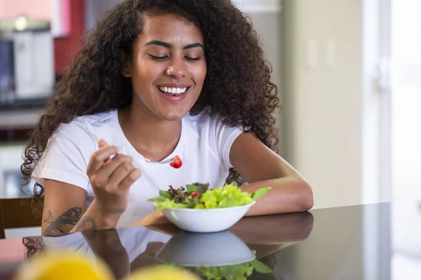 Jovem mulher afro-americana alegre comer salada de legumes em casa cozinha - Imagem . — Fotografia de Stock