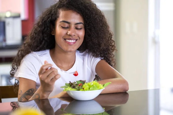Allegro giovane afro americano donna mangiare insalata di verdure in cucina a casa - Imagem . — Foto Stock