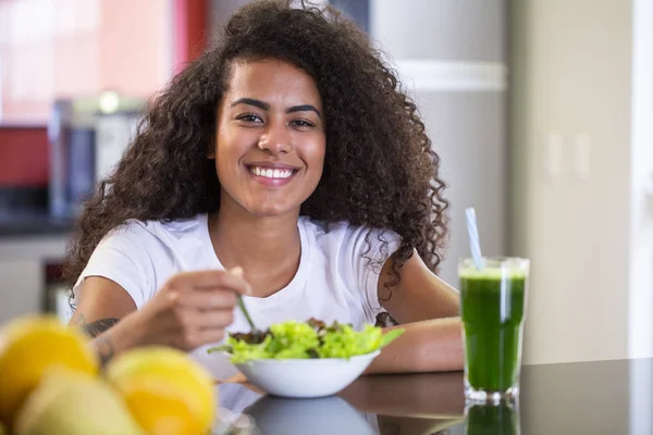 Allegro giovane donna afro americana mangiare insalata di verdure e succo di frutta verde in cucina di casa — Foto Stock