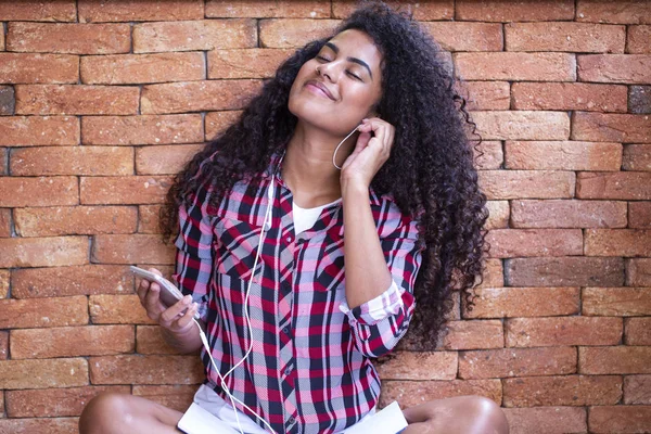 Encantadora joven afroamericana increíble, bailando mientras escucha música en auriculares en su teléfono móvil. Vestido con blusa colorida — Foto de Stock