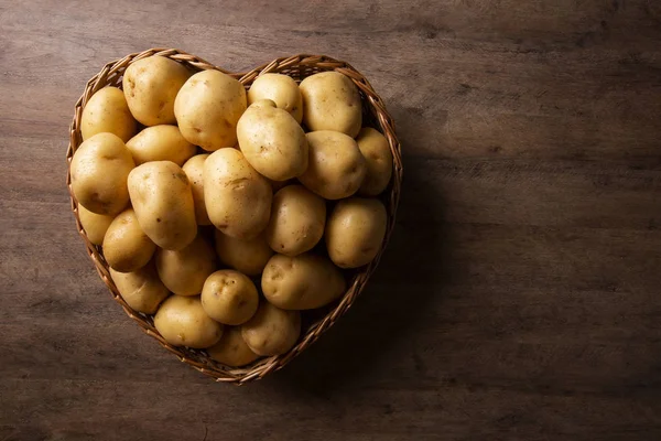 Many of potatoes in the heart basket on wooden background