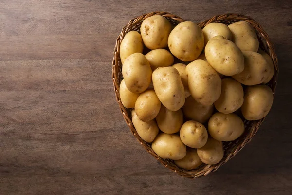 Many of potatoes in the heart basket on wooden background — Stock Photo, Image